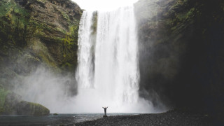 A huge waterfall in the background and a small figure standing at the bottom, raising their arms.